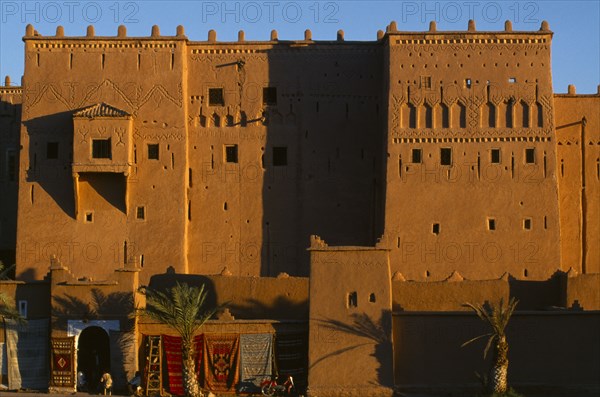 MOROCCO, Ouarzazate, View of red stone kasbah exterior with carpets hanging from the lower walls.