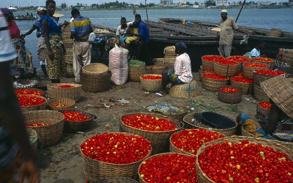 BENIN, Cotonou, Grand Marche de Dantokpa at the waters edge.  Baskets of red peppers, people and wooden boats moored behind.