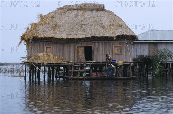 Benin, Ganvie, Thatched house on stilts in West African lake town, woman and children on a boat beside it.