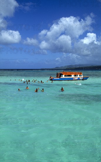 West Indies, Caribbean, Tobago, Tourists swimming in the shallow water beside a glass bottomed boat in the Nylon Pool in Buccoo Reef a coral reef in the marine park.