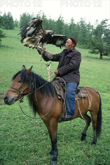 China, Xinjiang Province, Altay Mountains, Kazakh falconer on horseback with eagle used for hunting.