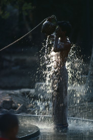 Myanmar, Myinkaba Village, Boy bathing outdoors in village near Pagan with sunlight catching the splashing water.