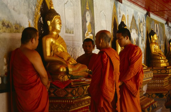 Thailand, Chiang Mai, Buddhist monks at Wat Doi Suthep praying on behalf of a family beside seated golden Buddha figure.