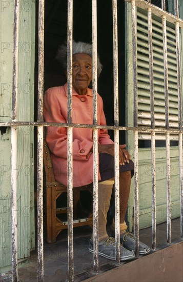 CUBA, Trinidad, Portrait of elderly woman sitting behind barred window.