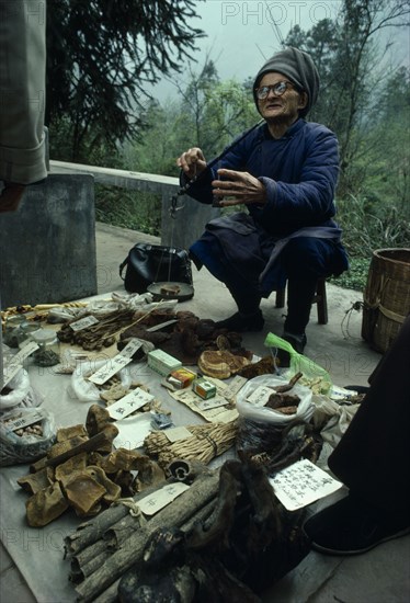 China, Sichuan Province, Mount Emei, Elderly man selling traditional Chinese medicines, using handheld scales to weight items for customer.