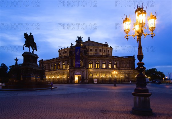 GERMANY, Saxony, Dresden, The restored Baroque Sachsische Staatsoper or State Opera House in Theatre Square first built in 1841 by architect Gottfried Semper illuminated at sunset with an equestrian statue of King Johann and an ornate lamppost in the foreground.