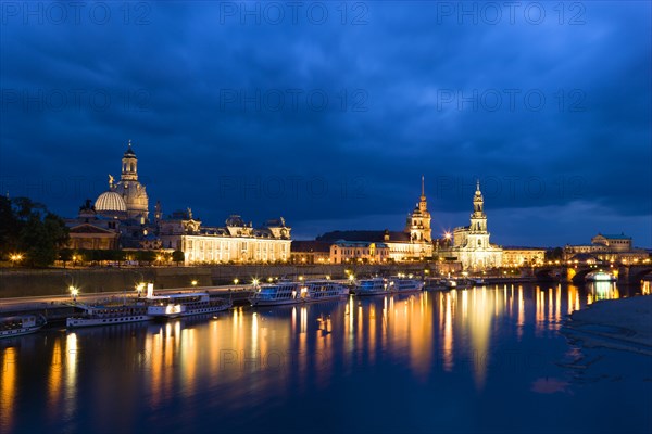 GERMANY, Saxony, Dresden, The city skyline at night with cruise boats moored on the River Elbe in front of the illuminated embankment buildings on the Bruhl Terrace of the Art Academy, the restored Baroque Frauenkirche Dome, the Residenzschloss, the Cathedral of Saint Trinitatis, and the Opera House.