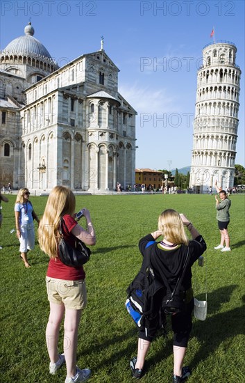 ITALY, Tuscany, Pisa, Campo dei Miracoli or Field of Miracles Tourists in front of the Duomo Cathedral and Leaning Tower belltower or Torre Pendente photographing each other pretending to hold the tower upright.