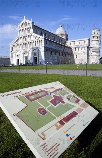 ITALY, Tuscany, Pisa, Campo dei Miracoli or Field of Miracles with a map guide on the grass of the Piazza del Duomo with the Duomo Cathedral church and  Leaning Tower belltower or Torre Pendente with tourists under a blue sky.