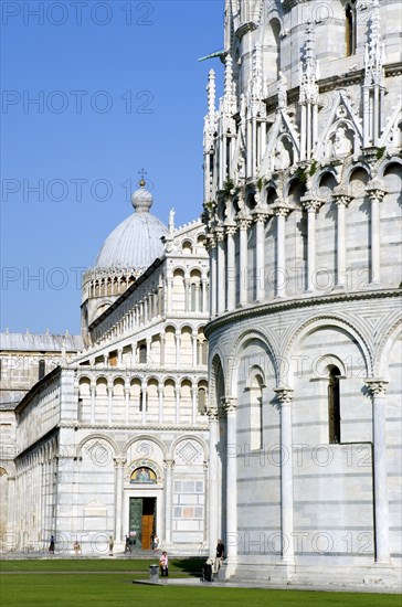 ITALY, Tuscany, Pisa, Campo dei Miracoli or Field of Miracles The Duomo Cathedral and Baptistry under a blue sky with tourist walking at their base.