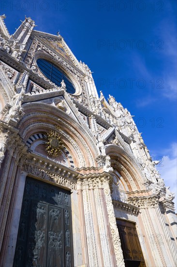 ITALY, Tuscany, Siena, The pink black and white marble facade of the Duomo cathedral church of Santa Maria Assunta under a blue sky.