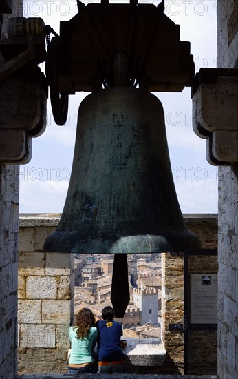ITALY, Tuscany, Siena, Palazzo Publico Two young tourists at the top of the Torre del Mangia campanile belltower beneath a large bronze bell looking out over the city.