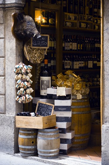 ITALY, Tuscany, Siena, Shop doorway display of Chianti wines and pasta with a stuffed wild boar head on the wall.
