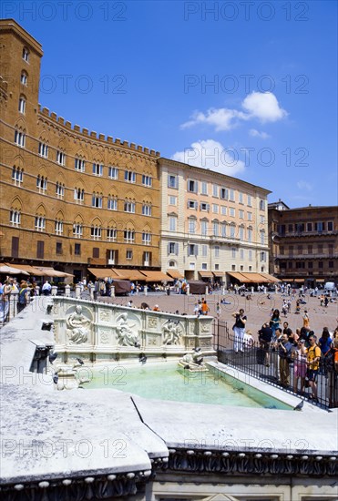 ITALY, Tuscany, Siena, Tourists around the 19th Century replica of the 15th Century white marble Fonte Gaia fountain by the artist Jacopo della Quercia in the Piazza del Campo with the square beyond.