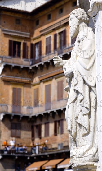 ITALY, Tuscany, Siena, Religious carving at the entrance to the Palazzo Publico in the Piazza del Campo with people on balconies beyond.