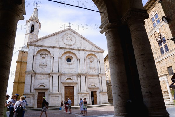 ITALY, Tuscany, Pienza, Val D'Orcia The Duomo in Piazza Pio II seen through an arch with tourists walking in the square. Built in 1459 by the architect Rossellino for Pope Pius II.