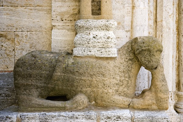 ITALY, Tuscany, San Quirico D'Orcia, The Collegiata Church of the saints Quirico and Giulitta. Sandstone carving of a lion, possibly Etruscan, at the base of a caryatid or zoomorphic column of the entrance to the church.