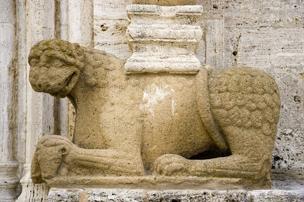 ITALY, Tuscany, San Quirico D'Orcia, The Collegiata Church of the saints Quirico and Giulitta. Sandstone carving of a lion, ossibly Etruscan, at the base of a caryatid or zoomorphic column at the entrance to the church.