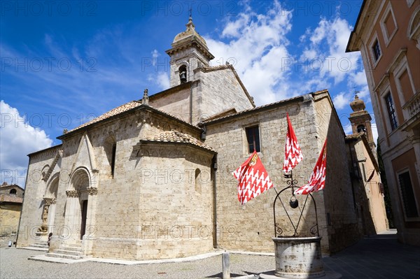 ITALY, Tuscany, San Quirico D'Orcia, The Collegiata Church of the saints Quirico and Giulitta. Flags of the Castello Quartieri or quarter of the medieval town decorate the water well in the square beside the church.