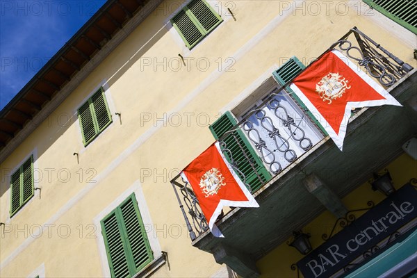 ITALY, Tuscany, San Quirico D'Orcia, Shuttered window facade and balcony of the Bar Centrale in the main square decorated with the red and white banner bearing the crest of the Castello Quartieri or quarter.