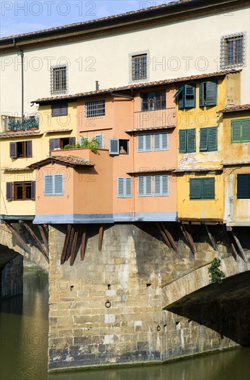 ITALY, Tuscany, Florence, Ponte Vecchio medieval bridge across River Arno with view of merchant's shops that line bridge and hang over the water below.