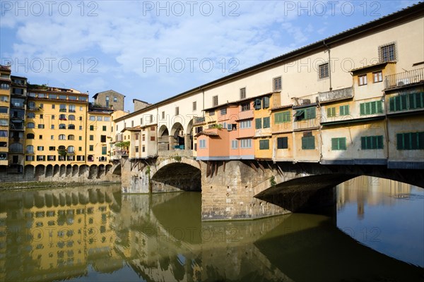 ITALY Tuscany Florence Ponte Vecchio medieval bridge across River Arno with view of merchant's shops that line bridge and hang over the water below.