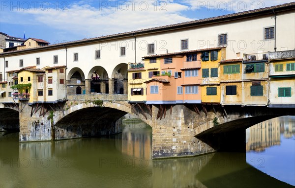 ITALY Tuscany Florence Ponte Vecchio medieval bridge across River Arno with view of merchant's shops that line bridge and hang over the water below.