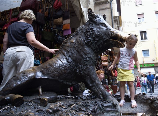 ITALY, Tuscany, Florence, People by the 17th century bronze fountain called Il Porcellino in the Mercato Nuovo also known as the Straw Market where the snout of the wild boar shines where people rub it under the superstition that if you do you will return to the city.