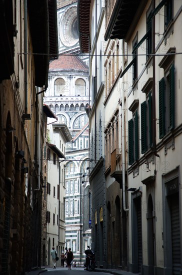 ITALY, Tuscany, Florence, The Cathedral of Santa Maria del Fiore with the marble sides of the church seen down a narrow street with people walking past.