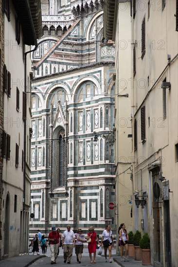 ITALY, Tuscany, Florence, The Cathedral of Santa Maria del Fiore with the marble sides of the church seen down a narrow street with people walking past.