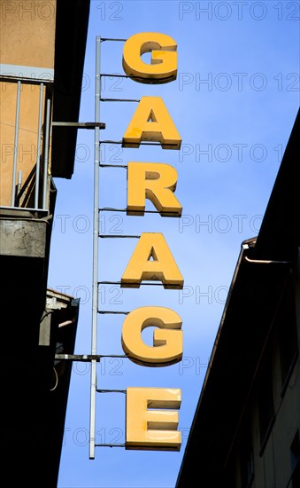 ITALY, Tuscany, Florence, Sign in yellow letters attached to building and hanging over street for a garage car park.