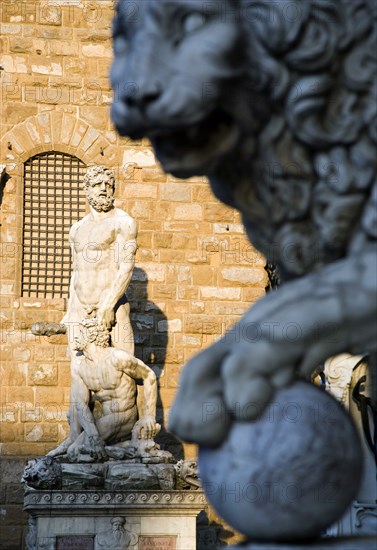 ITALY, Tuscany, Florence, The 1533 statue of Hercules and Cacus by Bandinelli seen through the legs of a stone lion outside the Loggia del Lancia or di Orcagna beside the Palazzo Vecchio in the Piazza della Signoria with a stone lion in the foreground.