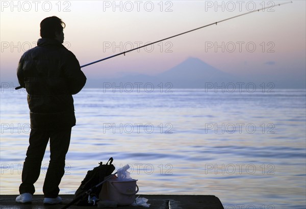 Japan, Honshu, Chiba, Tateyama, man fishing in Tokyo Bay, Mount Fuji visible across the water.