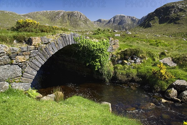 IRELAND, County Donegal, The Poisoned Glen, A stream runs under an old style stone bridge with the Derryveagh Mountain behind.