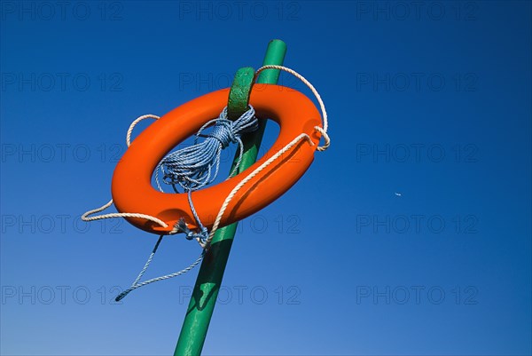 IRELAND, County Dublin, Howth, Red life belt on green stand with blue sky and plane behind.