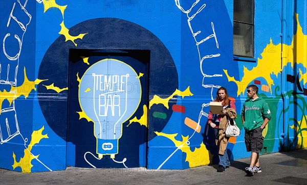 IRELAND, County Dublin, Dublin City, Temple Bar, Colourful artwork on a wall with two people walking by.