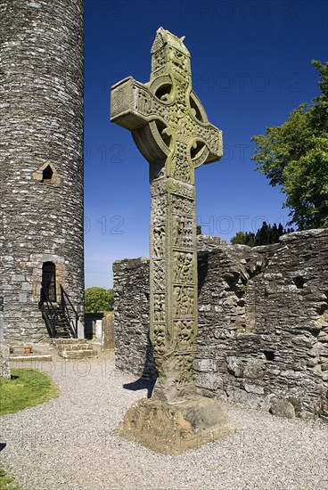 IRELAND, County Louth, Monasterboice Monastic Site, The West Cross is one of the tallest High Crosses in Ireland at 6.5 metres, angular view of east face with Round Tower in the background.