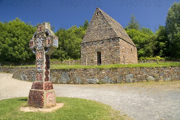 IRELAND, County Wexford, Irish National Heritage Park, Reconstruction of a typical monastic oratory with replica of a celtic cross in front.