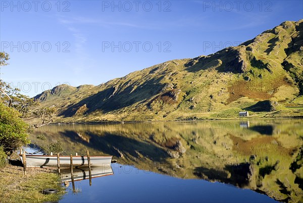IRELAND, County Galway, Connemara, Kylemore Lough with rowing boat and reflection of stone cottage.