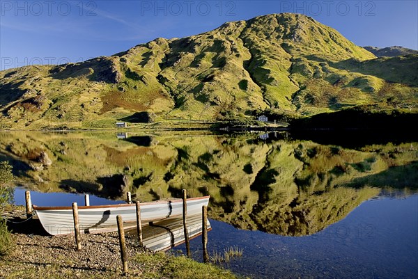 IRELAND, County Galway, Connemara, Kylemore Lough with moored rowing boat and Benbaun Mountain behind.