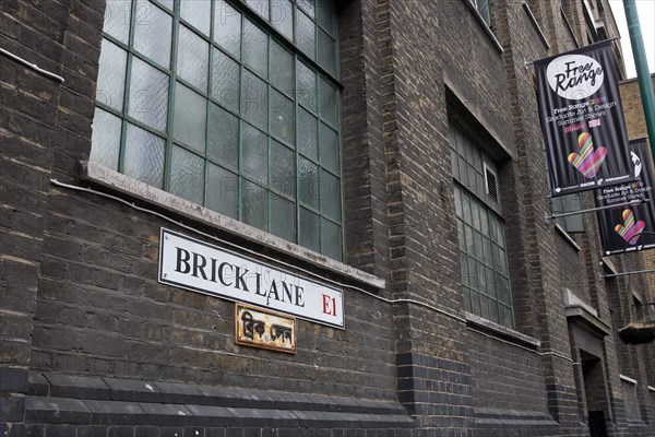 ENGLAND, London, East End, Whitechapel,  Brick Lane, Truman Black Eagle brewery brick wall with its big windows and the brick lane address sign in both english and arabic noticeable.