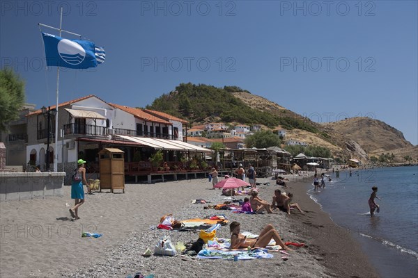 GREECE, North East Aegean, Lesvos Island, Eresos, View of beach with people sunbathing and swimming just in front of the villages bars and restaurants.
