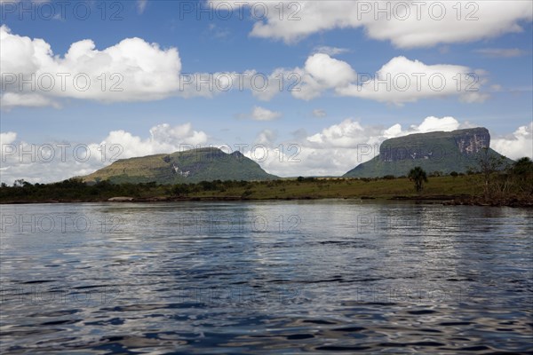 VENEZUELA, Bolivar State, Canaima National Park, River at the foreground, Savanna and Tepui mountains and white clouds with blue sky at the background.