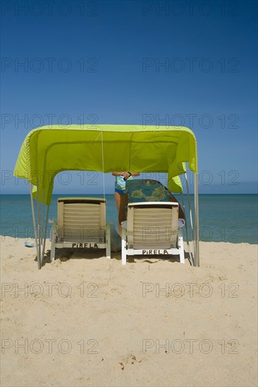 VENEZUELA, Margarita Island, Playa Caribe, View of a green tent at the Playa Caribe beach with a person reading the Margarita Islands map under the shade of the tent, just in front of the exotic seawater, shoot on a bright day with blue sky.