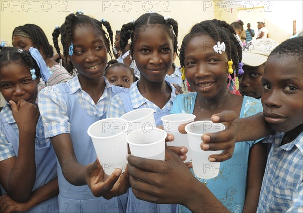 HAITI, Isla de la Laganave, School children holding plastic cups of water from plumbing paid for by Lemon Aid Scottish Charity.