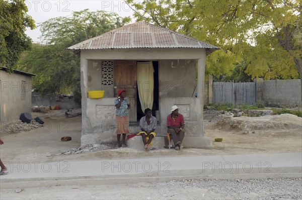 Haiti, Isla de Laganave, local people sat outside hime with tin roof.