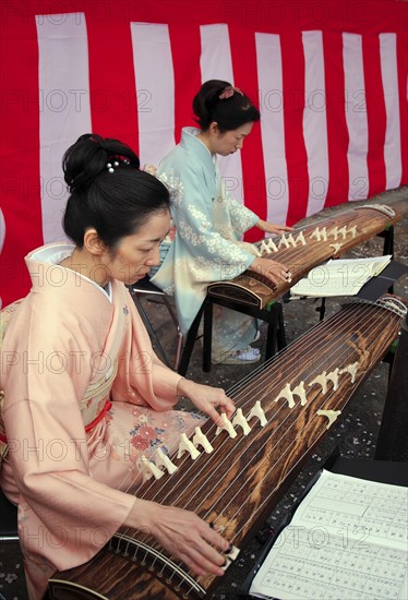 Japan, Tokyo, Meguro, beside the Meguro-gawa river, two women dressed in traditional kimonos playing Koto, traditional  instrument, horizontal harp, tradditional Japanese sheet music visible.