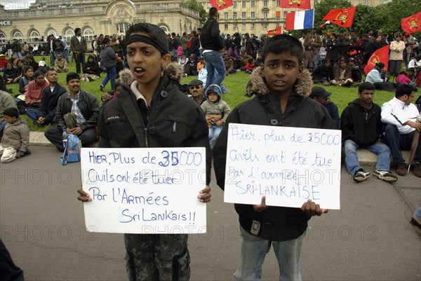 France, Paris, Esplanade des Invalides,Two boys stand in front of a protest of Tamil Tiger supporters, holding signs reading, Yesterday, more than 35000 civilians were killed by the Sri Lankan army, in protest to the war in northern Sri Lanka.