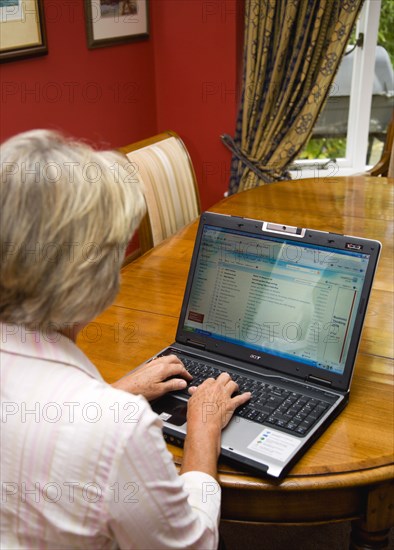 Industry, Computers, Laptop, Woman sitting at dining room table at home checking her email account on her laptop.