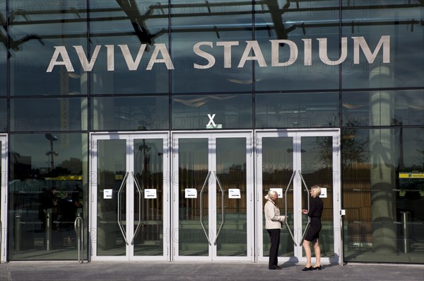 Ireland, County Dublin, Dublin City, Ballsbridge, Lansdowne Road, Women smoking outside the Aviva 50000 capacity all seater Football Stadium designed by Populus and Scott Tallon Walker. A concrete and steel structure with polycarbonate self cleaing glass exterior built at a cost of 41 million Euros. Home to the national Rugby and Soccer teams, aslo used as a concert venue.